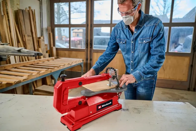 Ein Handwerker in einer Werkstatt nutzt eine rote Einhell Dekupiersäge, um präzise Holzarbeiten durchzuführen. Im Hintergrund sind Holzmaterialien und Werkstattelemente zu sehen. Ideal für DIY-Projekte und feine Sägearbeiten.